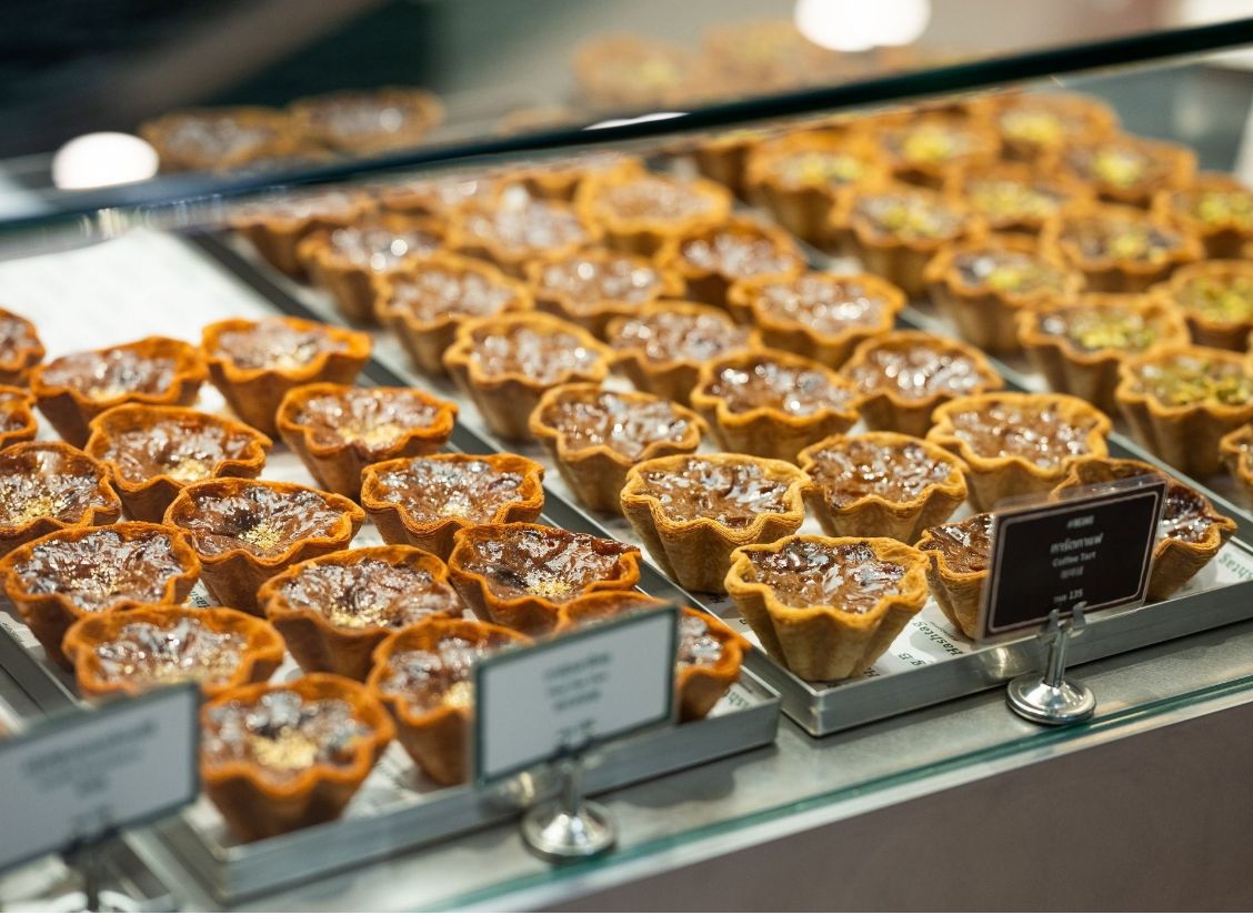 Rows of egg tarts with laminated pastry shells in a bakery display case